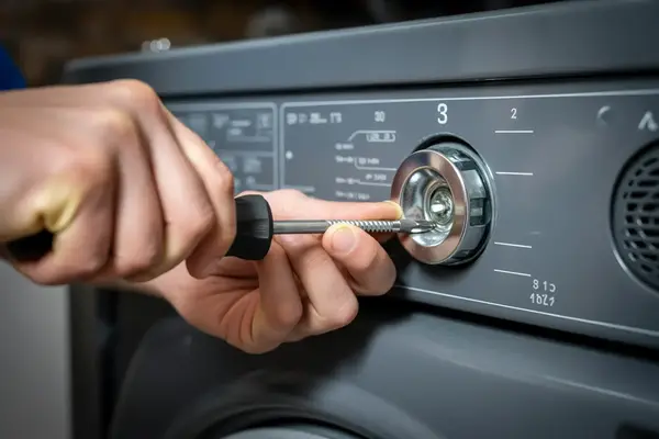 technician’s hands using a screwdriver to tighten a dryer panel screw